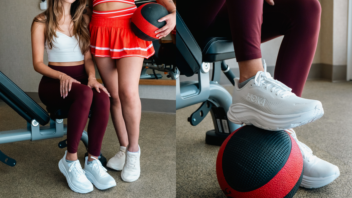 Two women in athletic wear at a gym, featuring white HOKA training shoes, with one foot resting on a red and black medicine ball.